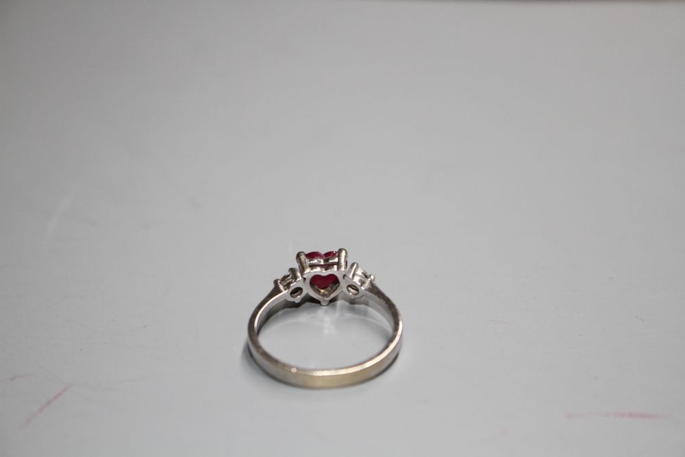 A modern 750 white metal, claw set heart shaped ruby and two round cut diamond set dress ring,